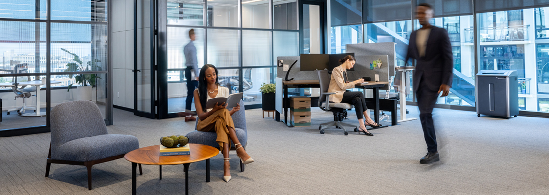 People working/walking in office setting. Large shredder in background.
