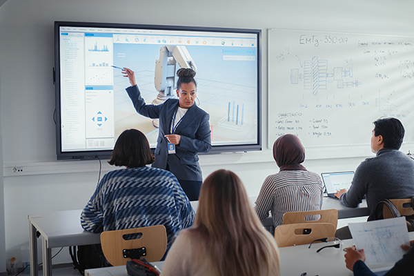 Teacher pointing at monitor on wall