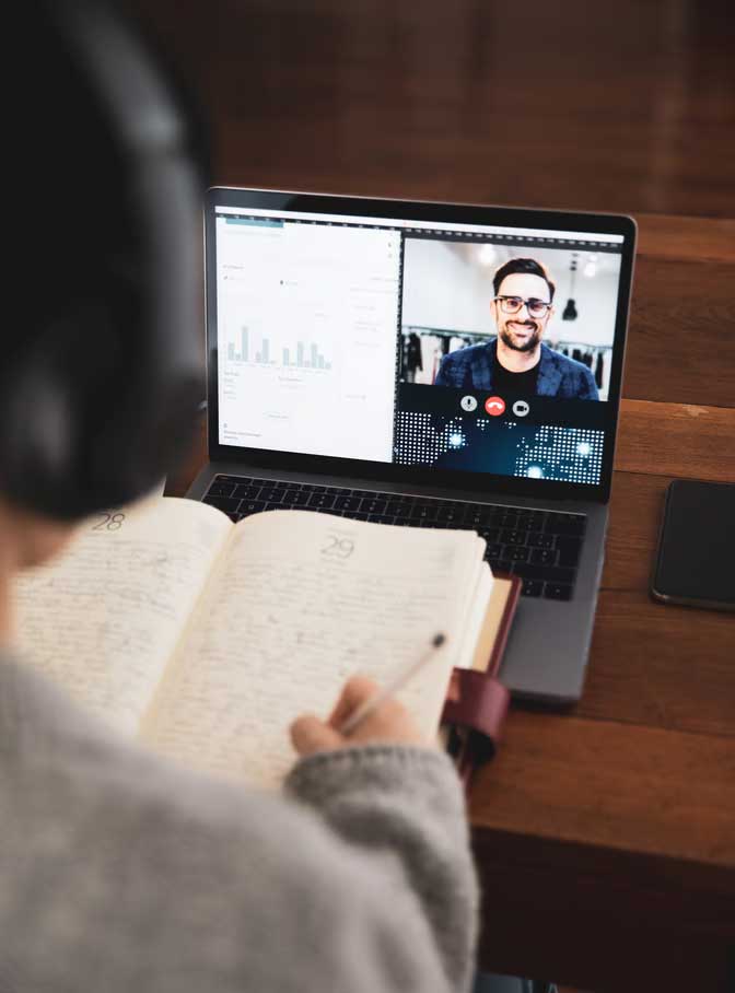 Student writing in notebook during zoom call with professor