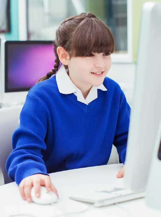 Young girl in blue sweater smiling while staring at her computer monitor