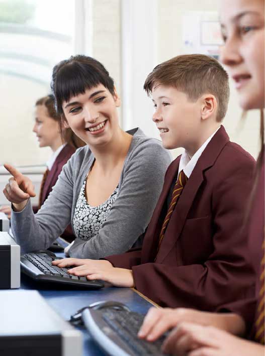 Female eacher helping young male student wearing school uniform at computer
